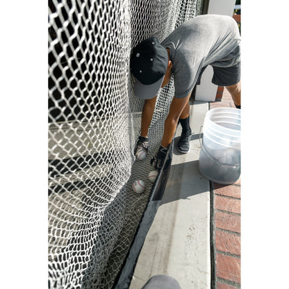 Person prepares baseballs against a fence outdoors for practice or training