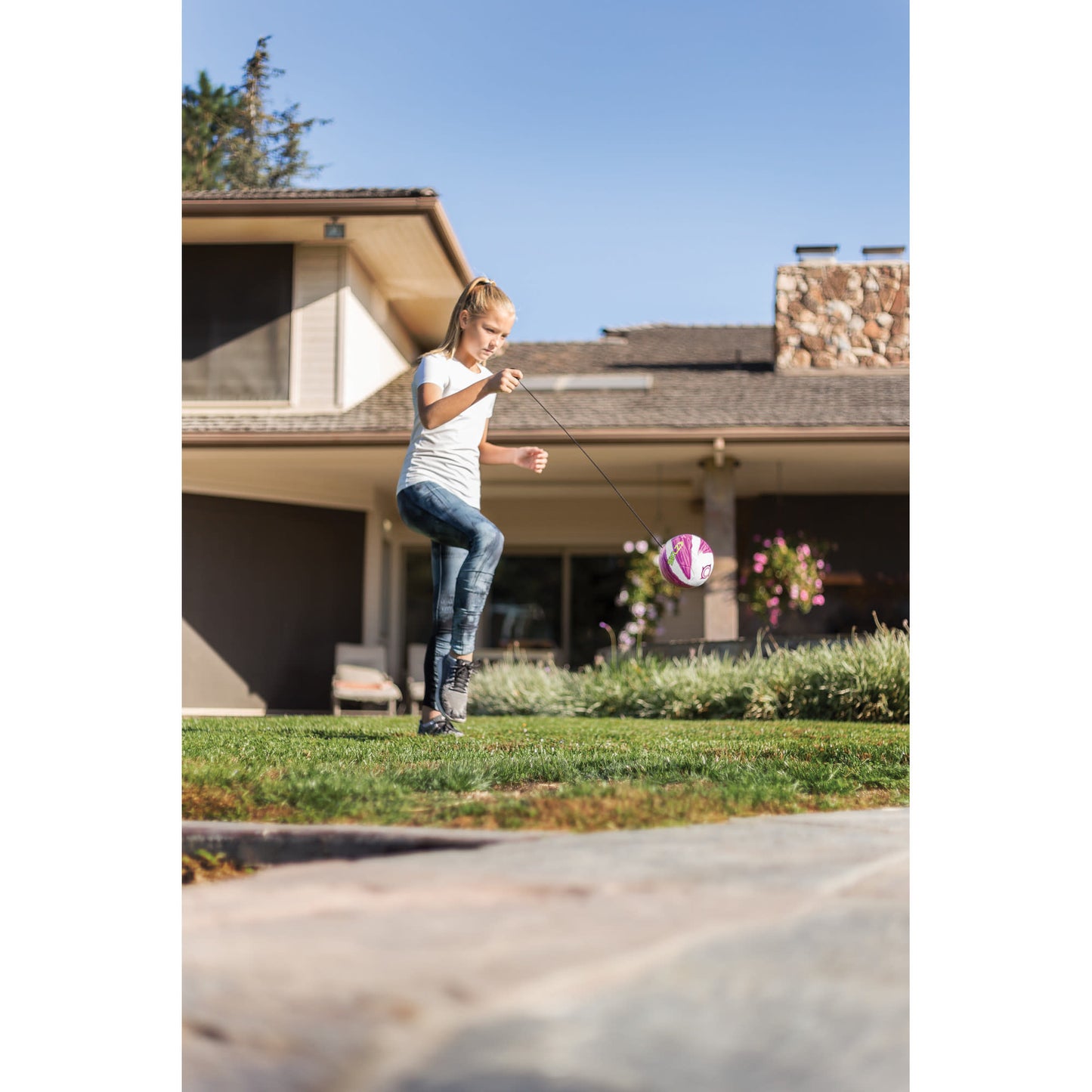 Girl swings a pink and white ball in a backyard garden near a house