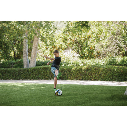 Boy kicks soccer ball on grass in park surrounded by trees and greenery