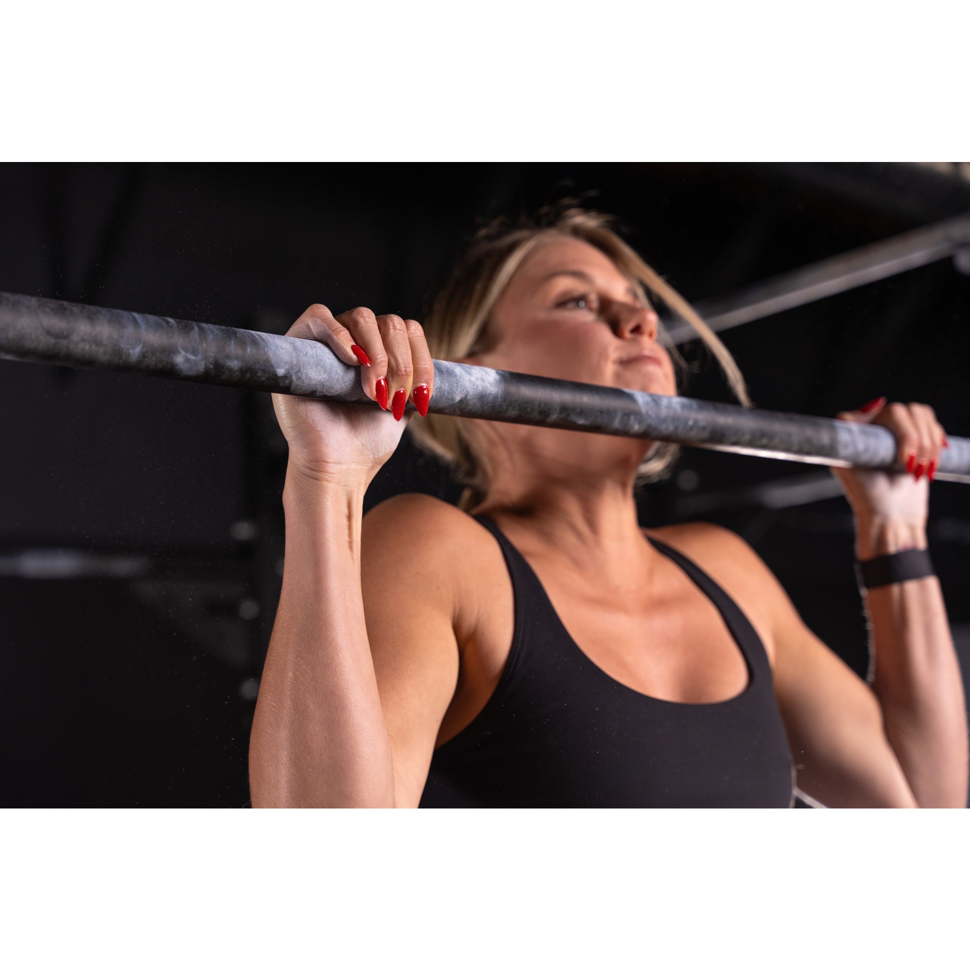 Woman pulls herself up on a gym bar, focused effort in a dimly lit fitness studio.