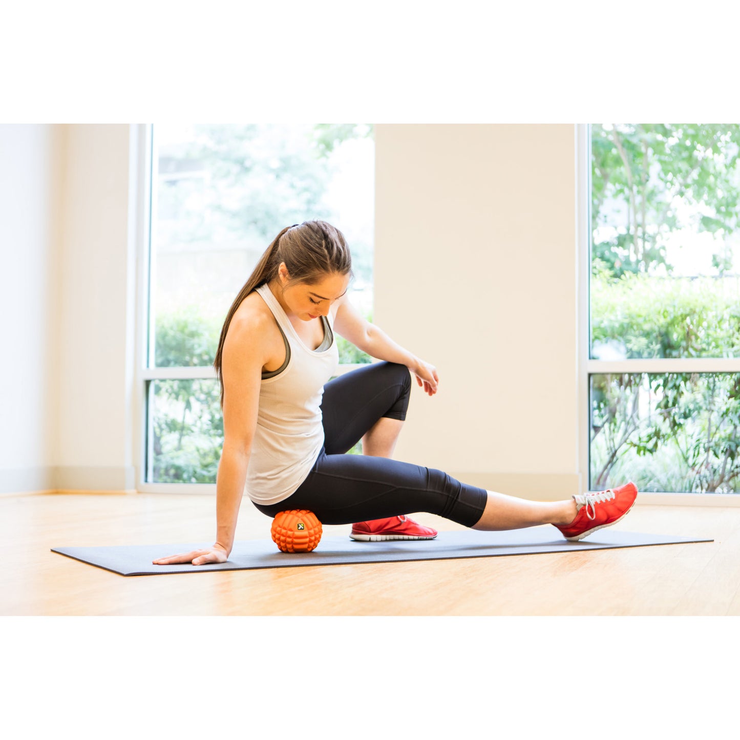 Woman stretches on a yoga mat indoors with a massage roller nearby.
