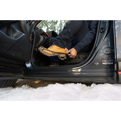 Person adjusts snowshoes inside vehicle on snowy ground at outdoor environment