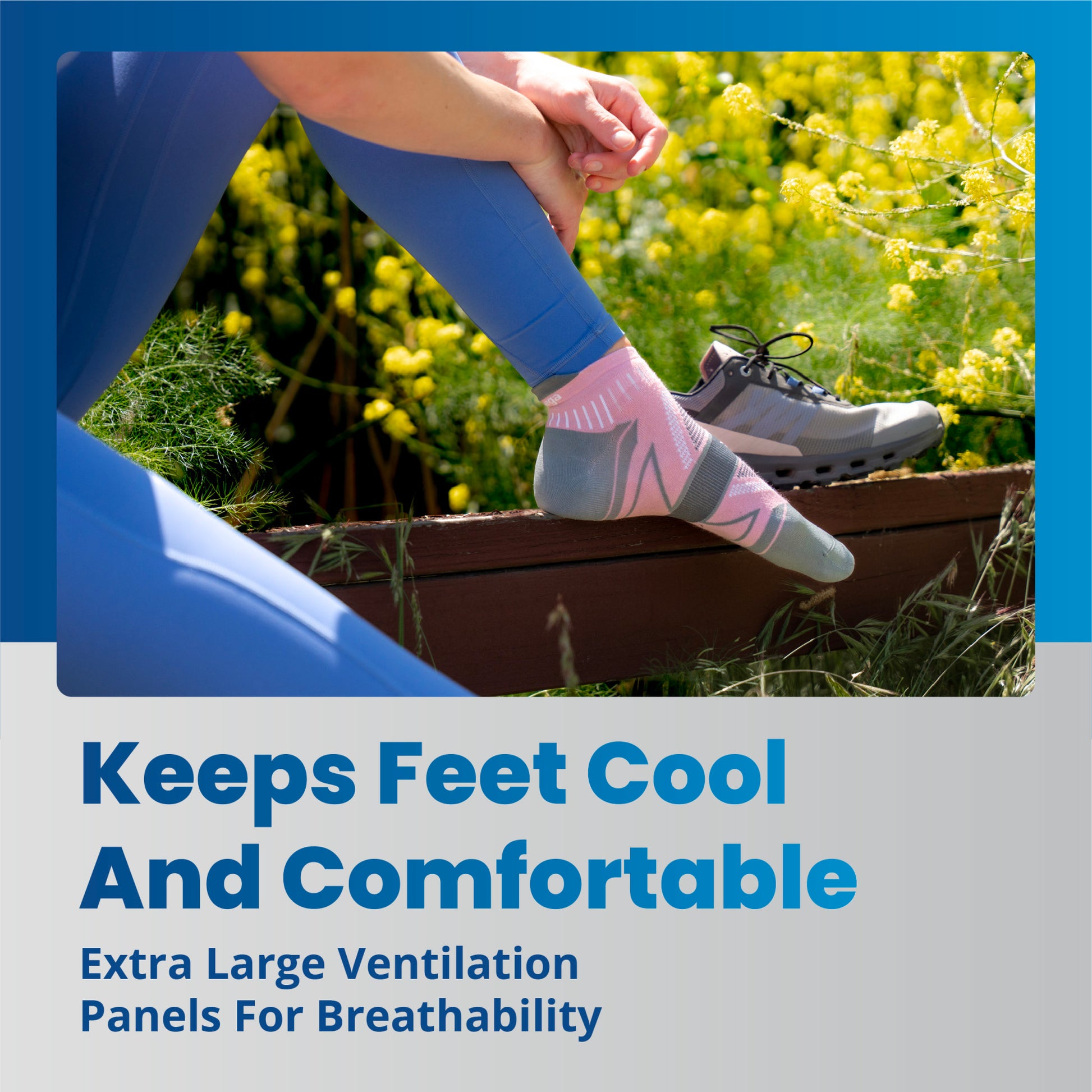 A person adjusts a sock on their foot while sitting outdoors surrounded by yellow flowers and greenery.