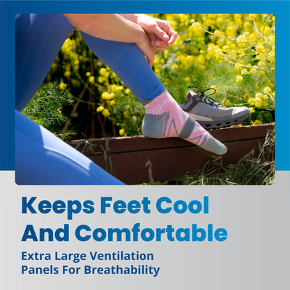 A person adjusts a sock on their foot while sitting outdoors surrounded by yellow flowers and greenery.