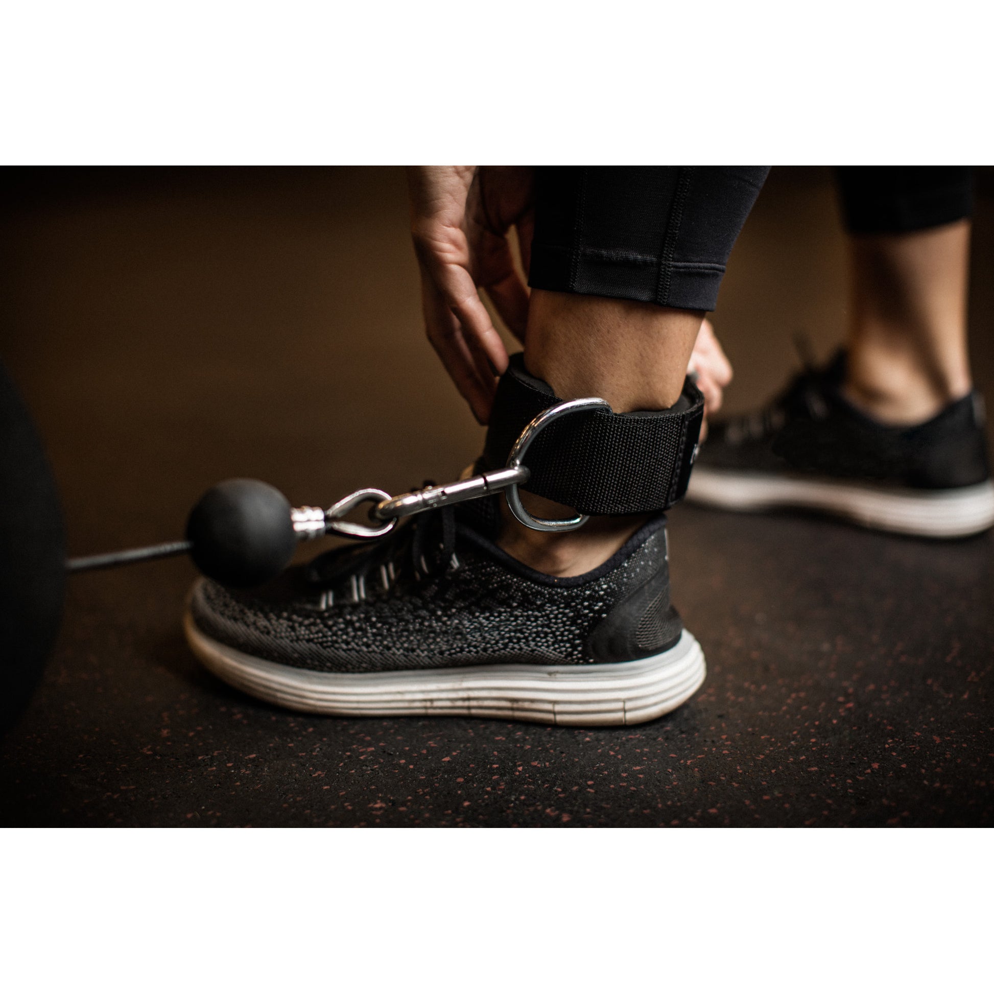 Person secures ankle weight with strap during workout in gym environment