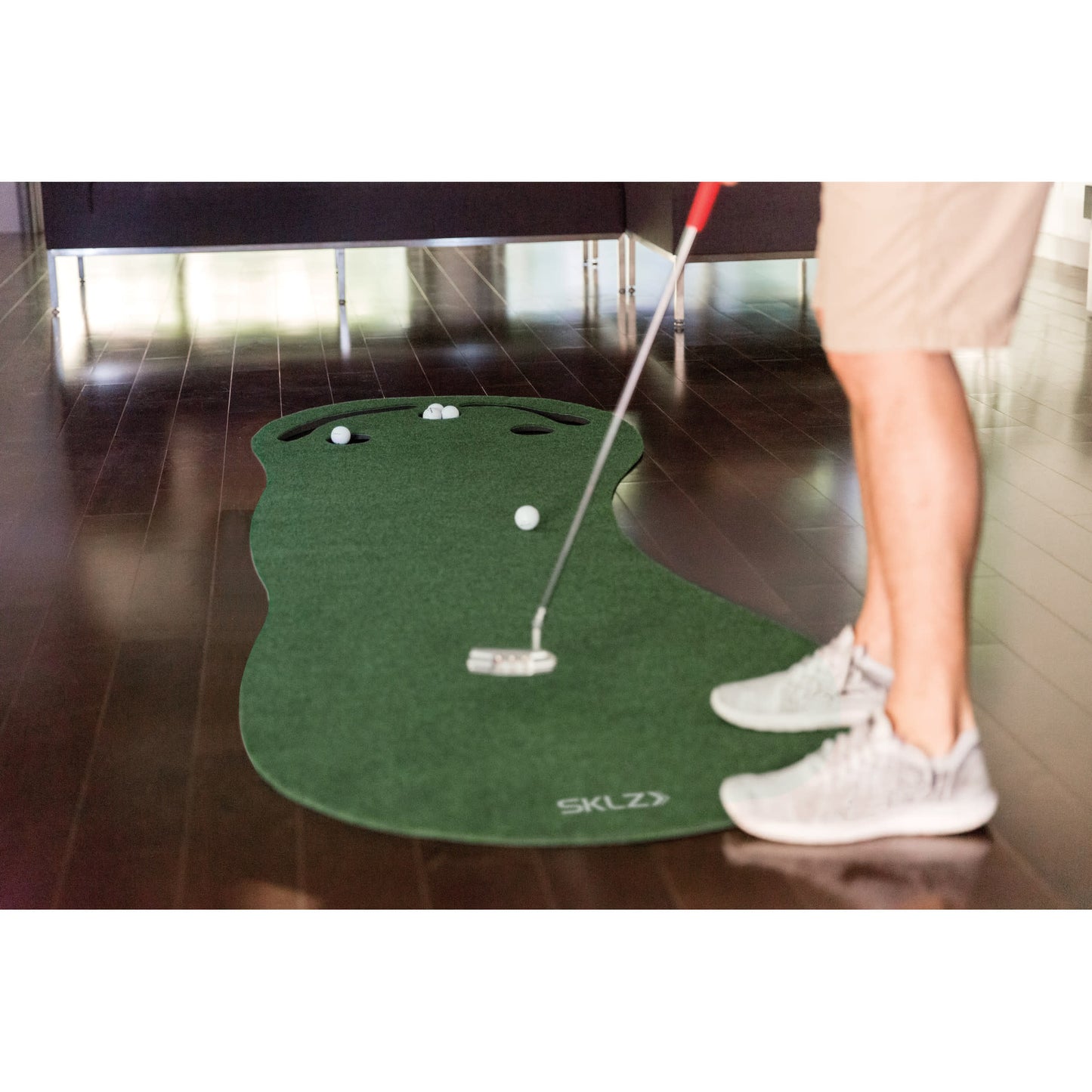 A person positions a putter on a golf mat with golf balls for indoor practice