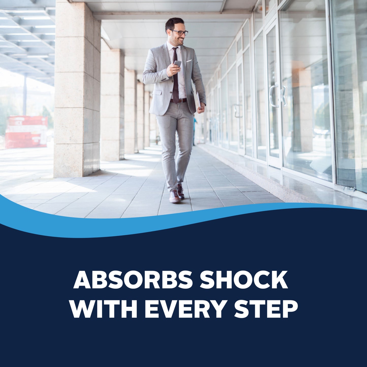 A man in a suit walks outside a building while looking at his phone, promoting shock absorption with each step.