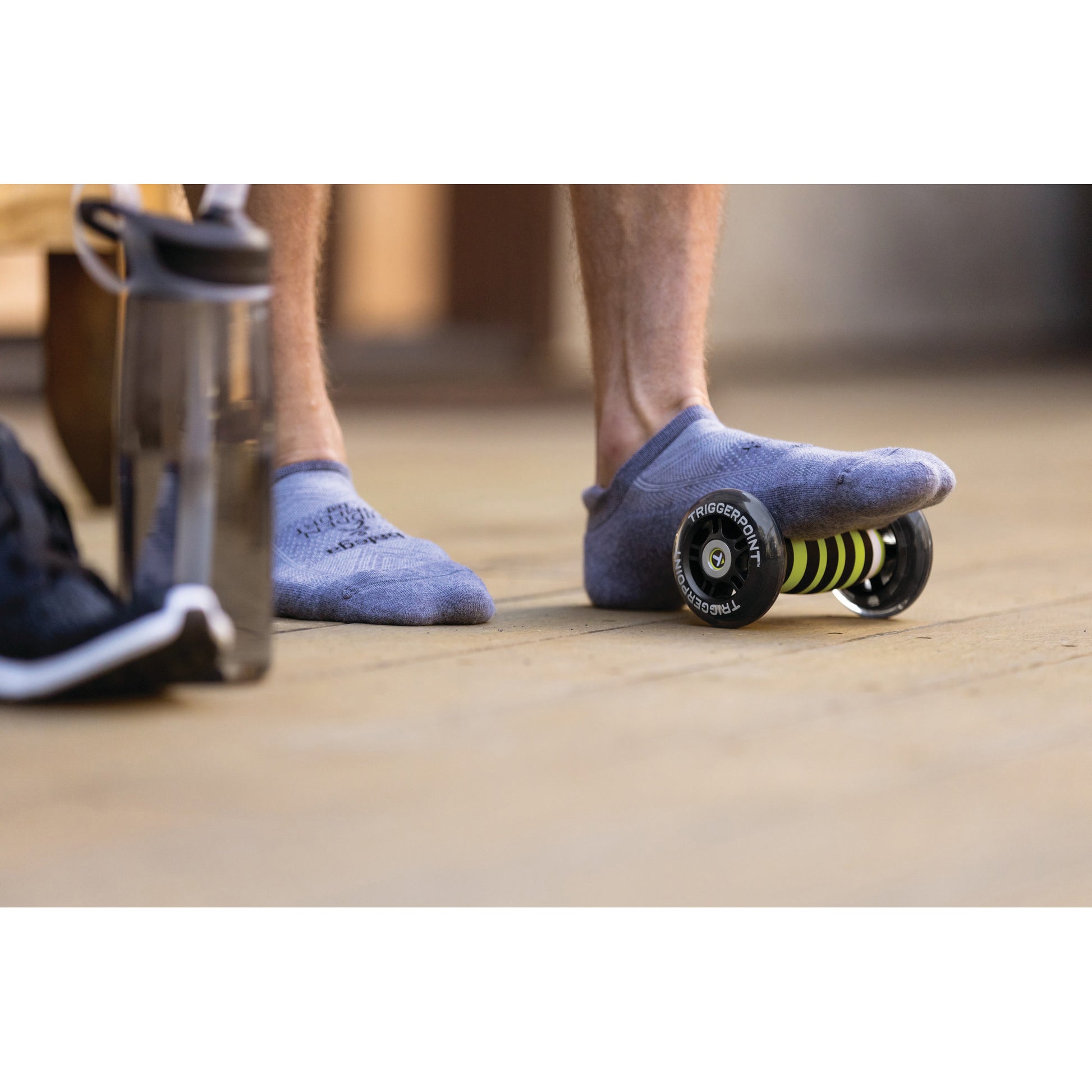 Person's foot on a skateboard in a gym with water bottle and bag nearby