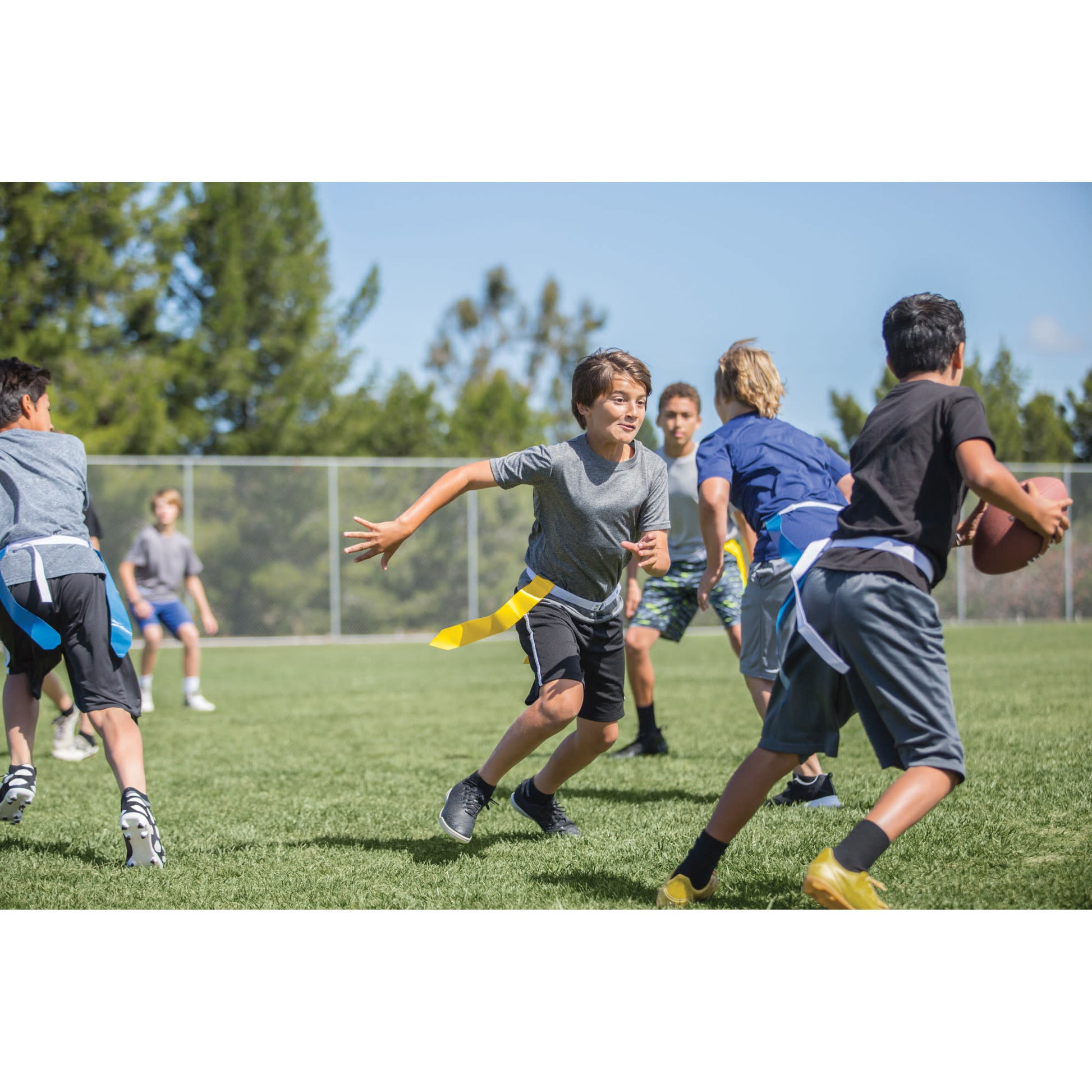 Kids run and chase a football on a grassy field during a game in an outdoor sports area