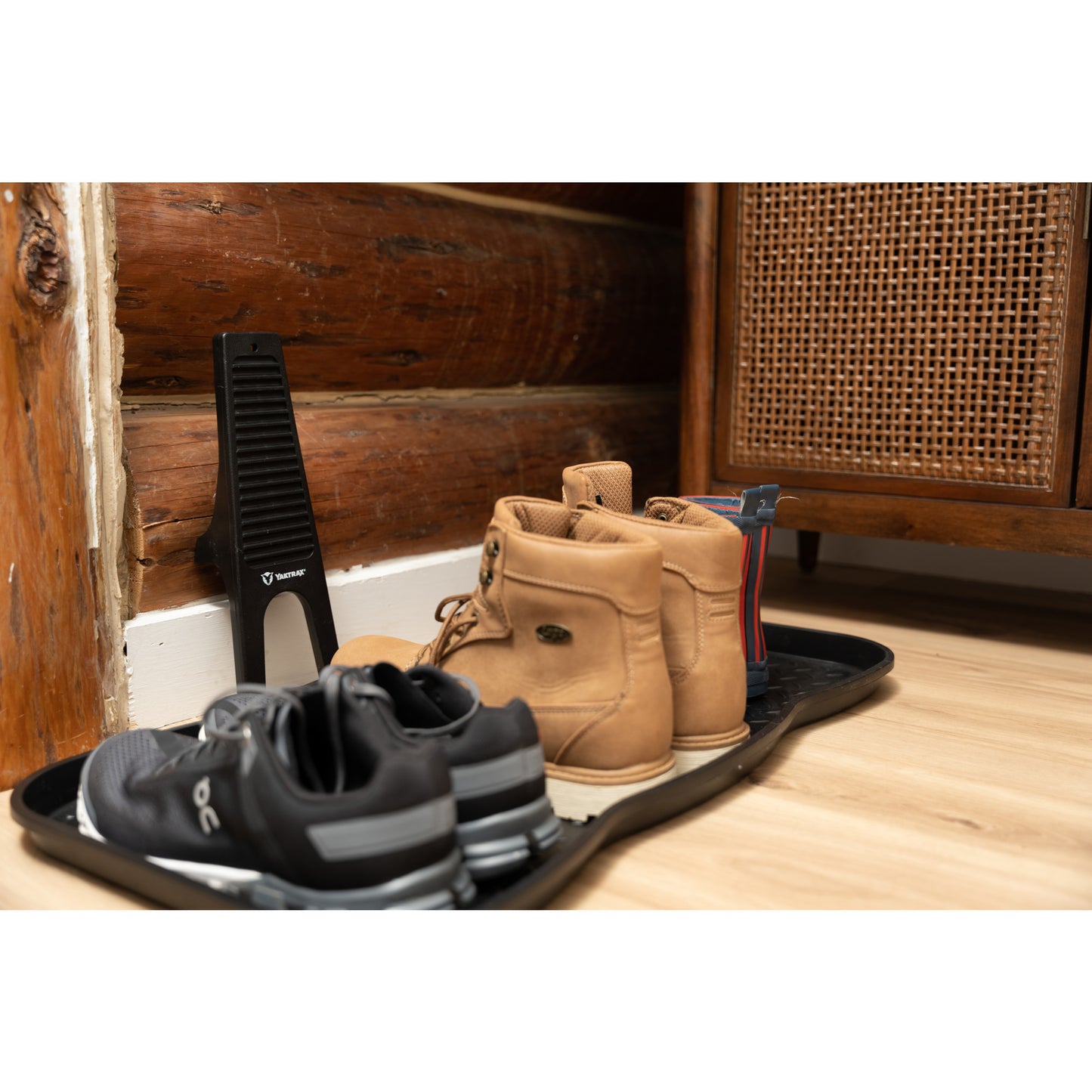 Shoes sit in a tray on the floor next to a wood wall and cabinet.