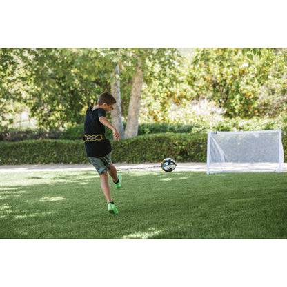 Boy kicks soccer ball on grass field with goalpost and trees in background