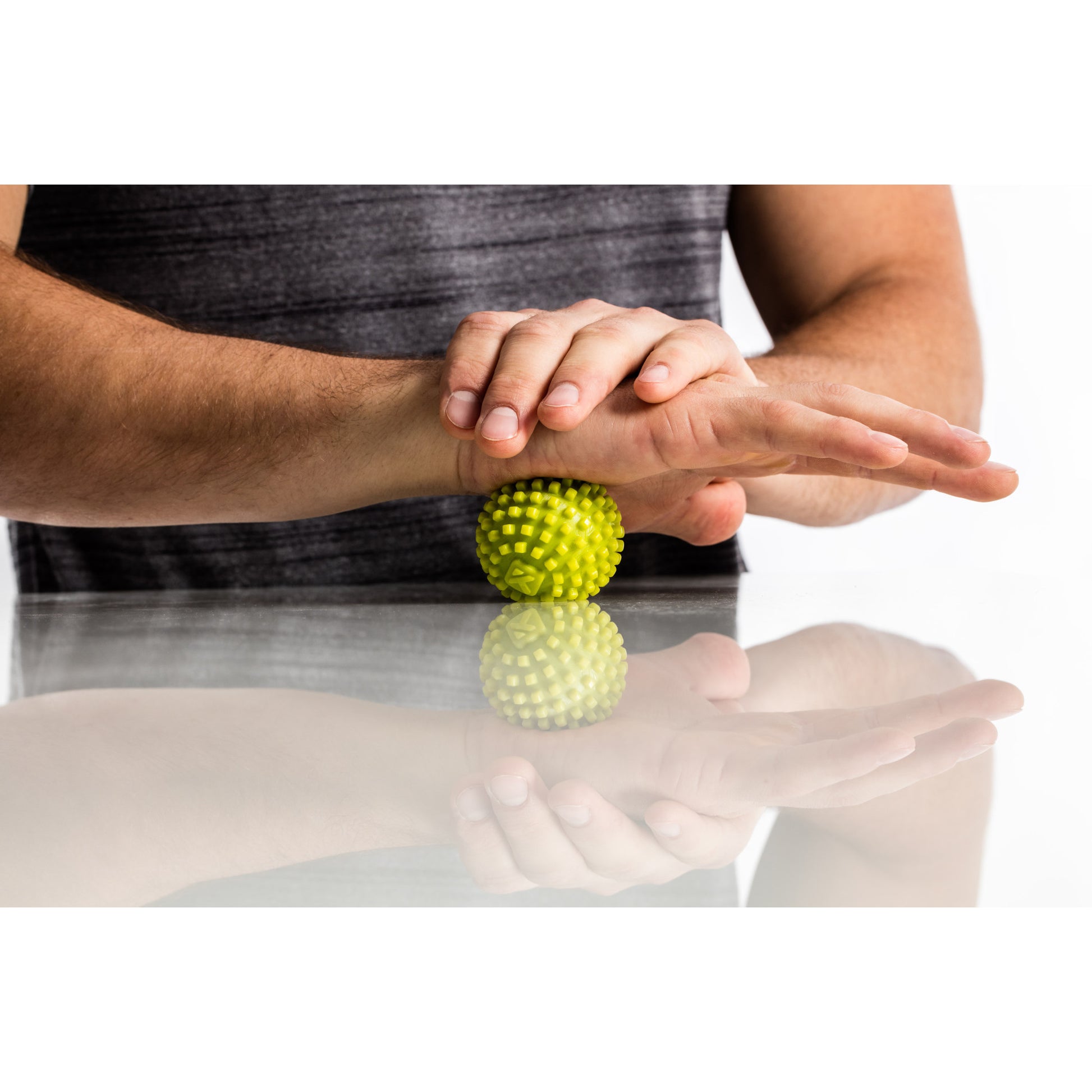 Hands balance on a spiky massage ball on a reflective surface in a wellness setting.