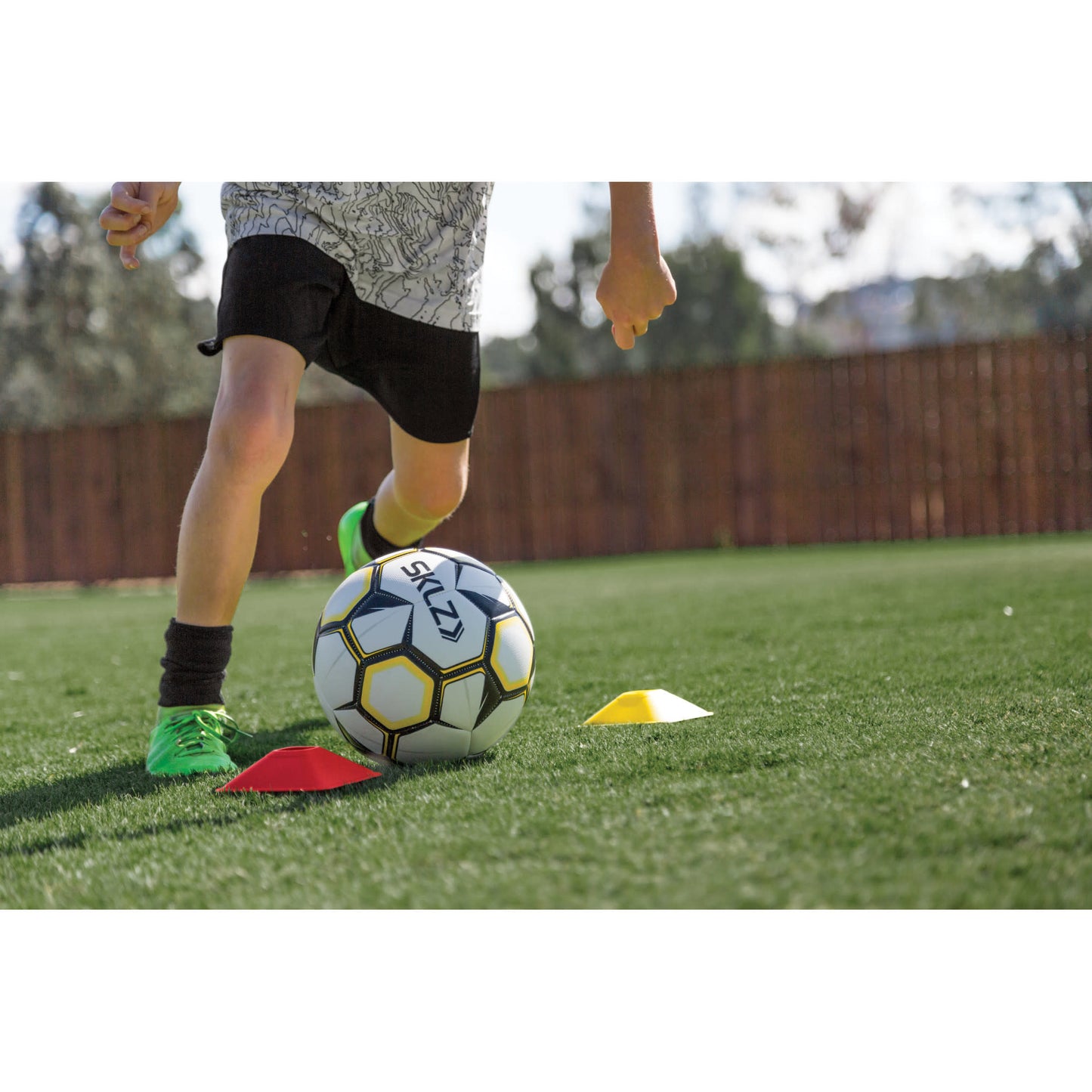 Child dribbles soccer ball around cones on a grassy field during training session