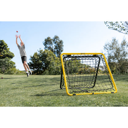 Child practices throwing a ball into the net outdoors on a grassy field.
