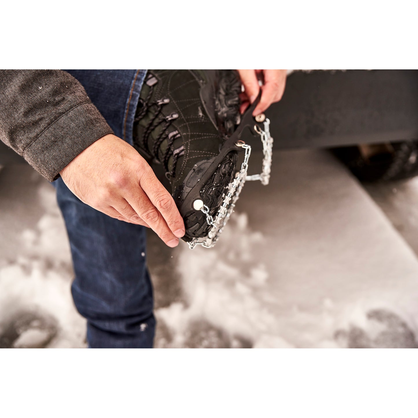 Person adjusts snowshoe on boot outdoors with snow on the ground