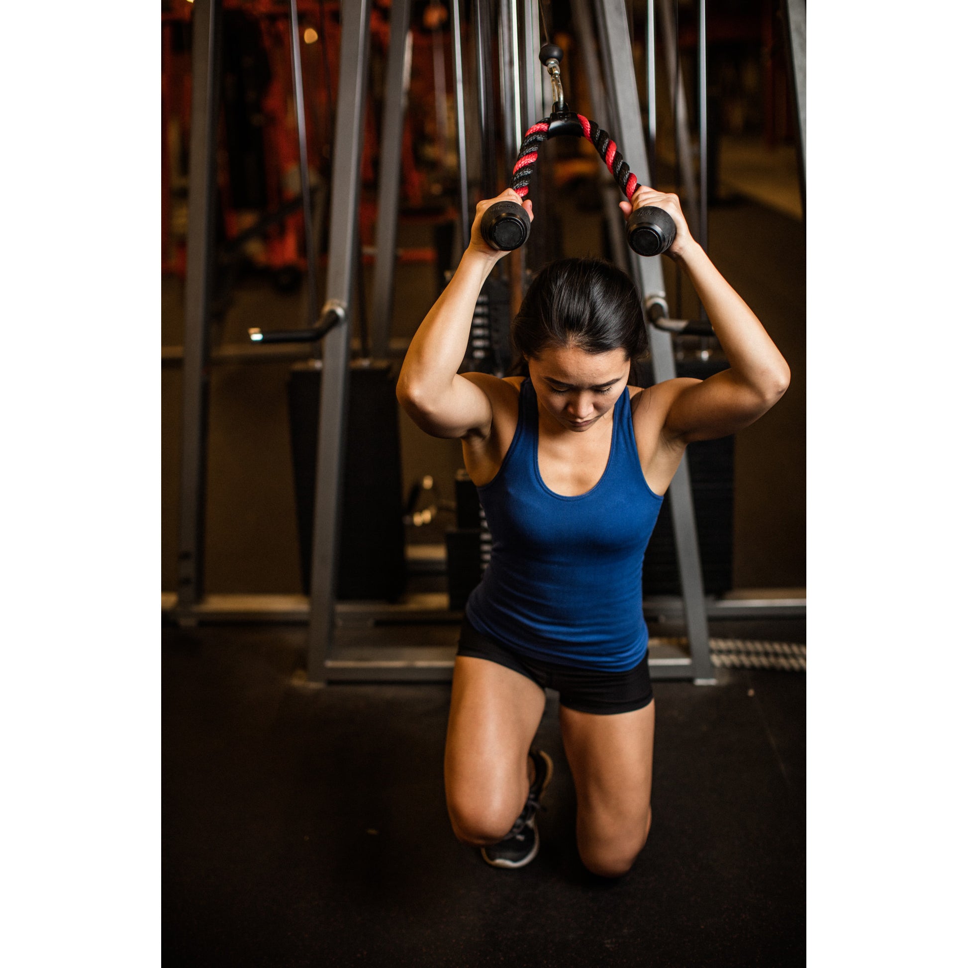 Person kneeling, pulling cable, focused in gym setting.