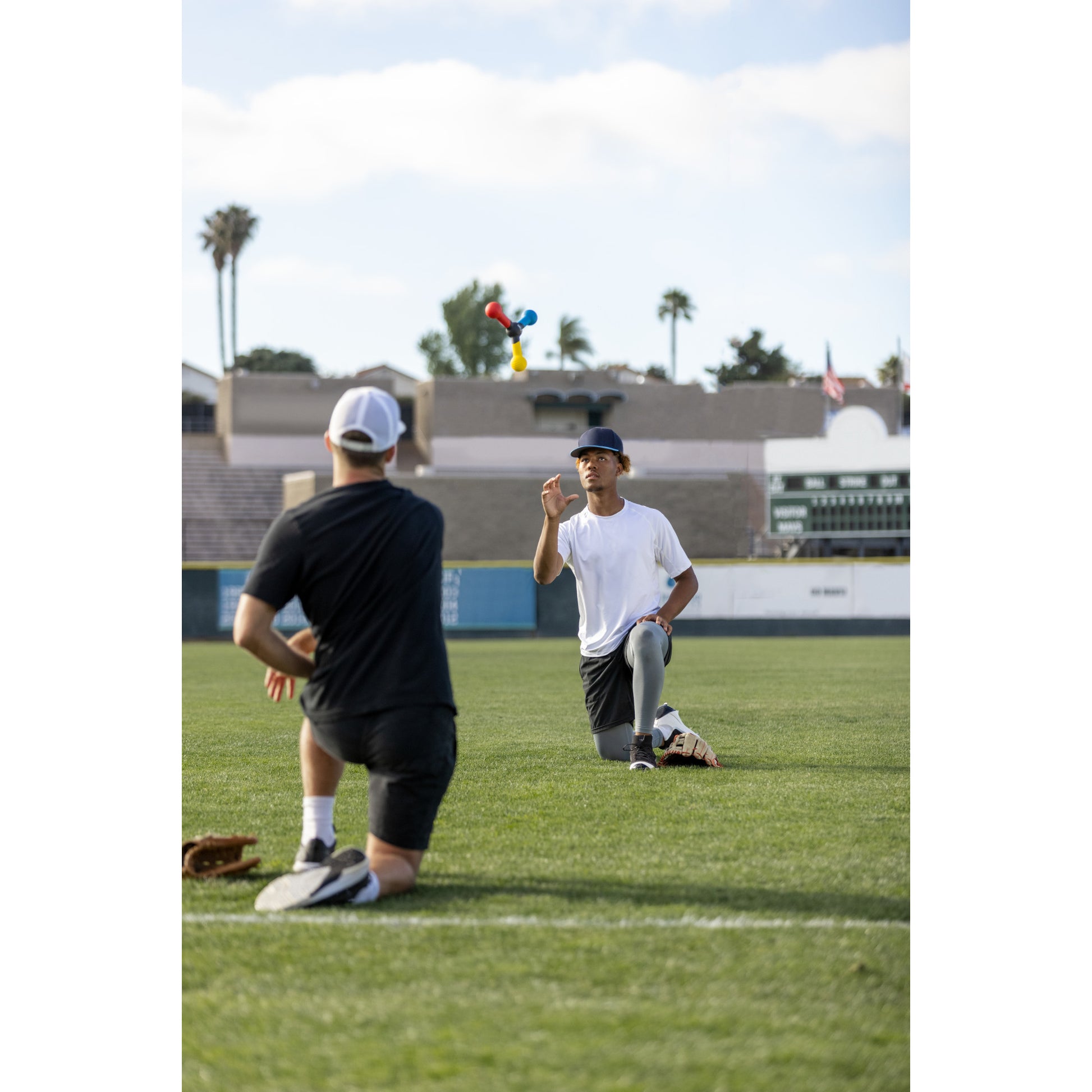 Two people rehearse a speech on a baseball field with a stuffed toy in the background