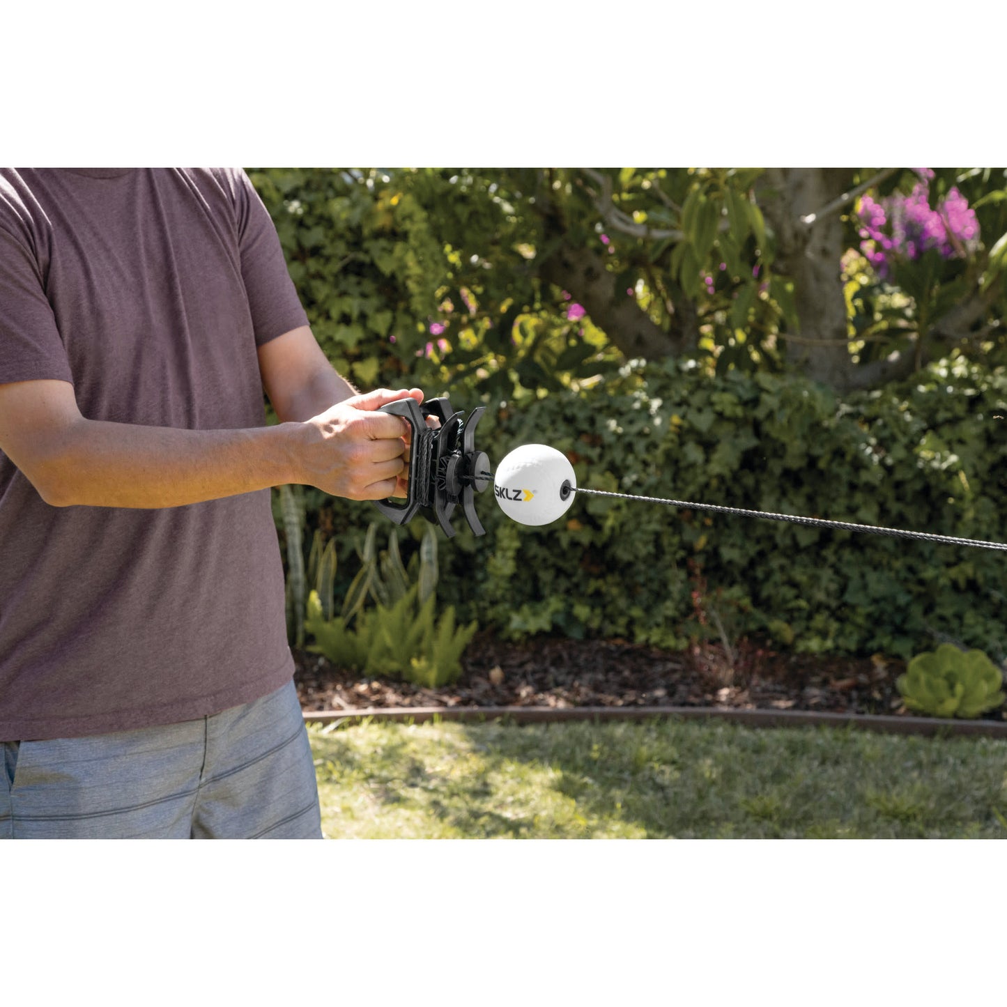 Person holds a buoyant underwater drone with a cable outdoors near plants and trees