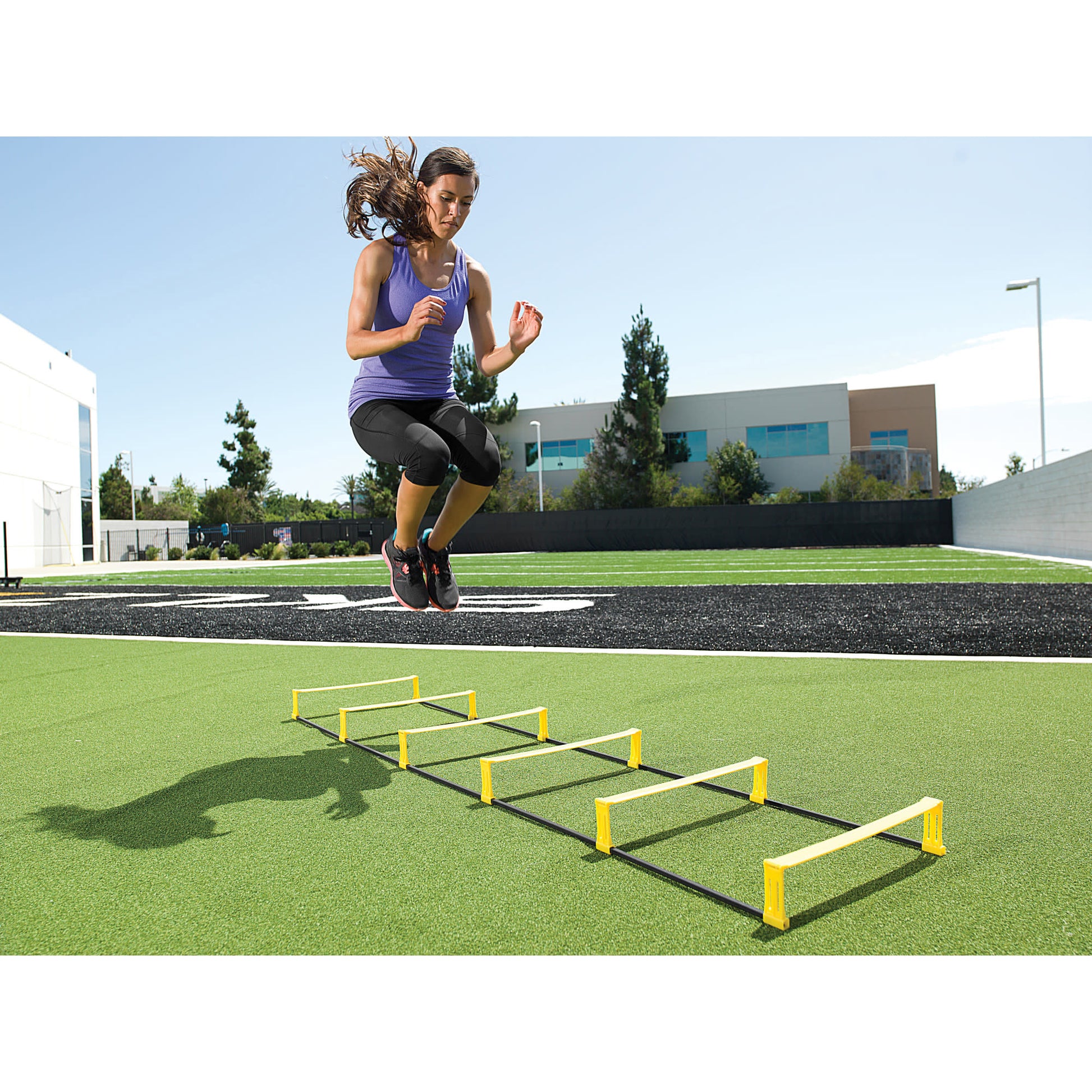 Athletic woman jumps over agility hurdles on a sports field outdoors