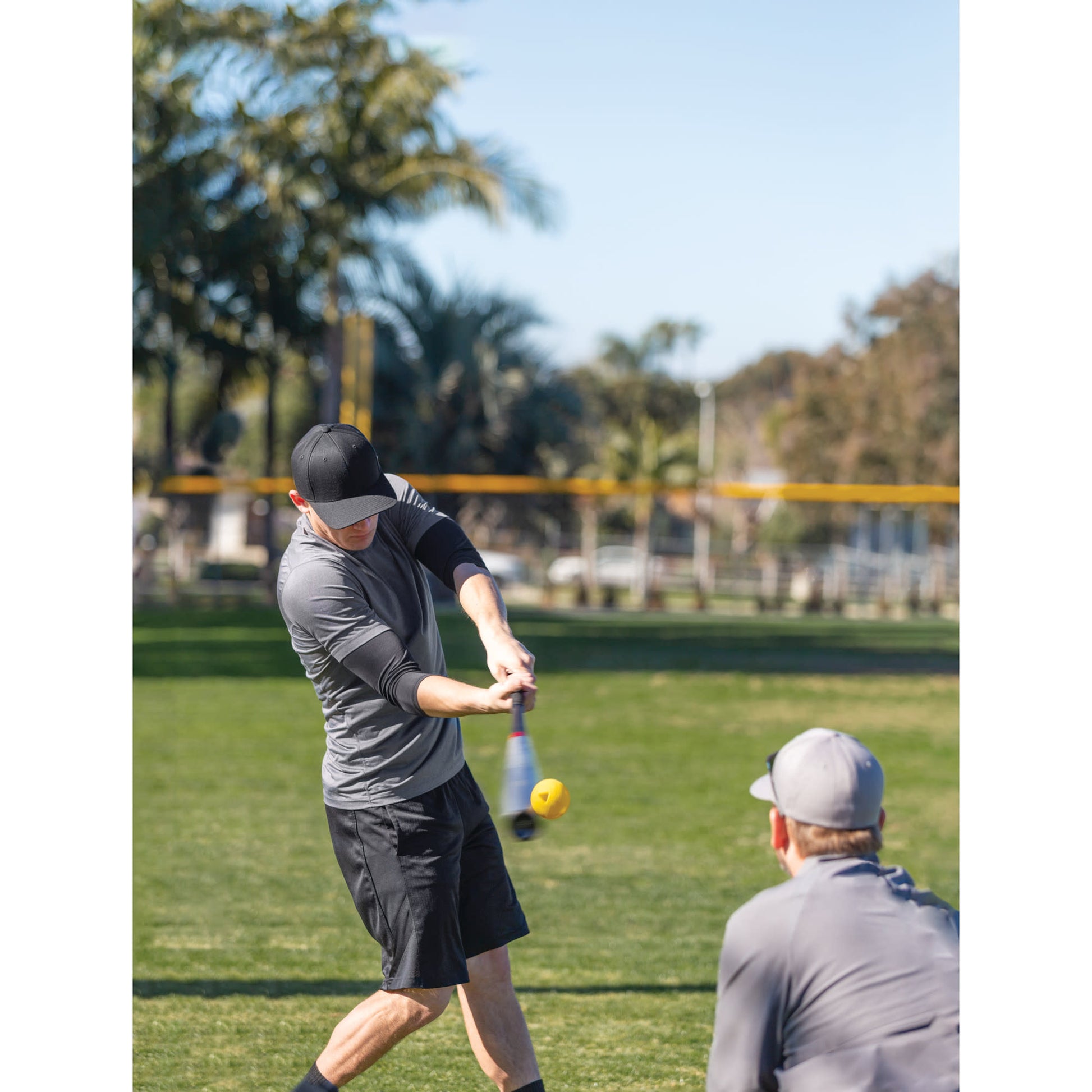 Boy swings golf club on grass field with man watching nearby in sunny outdoor park