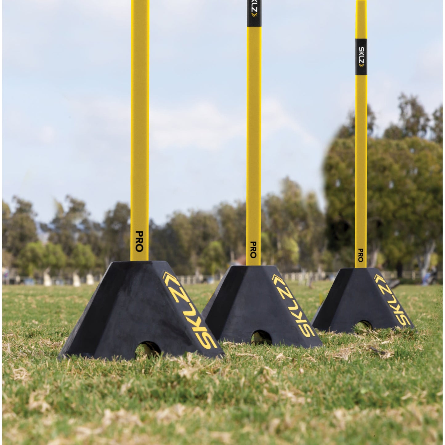 Three black agility barriers with yellow poles on grassy field under blue sky