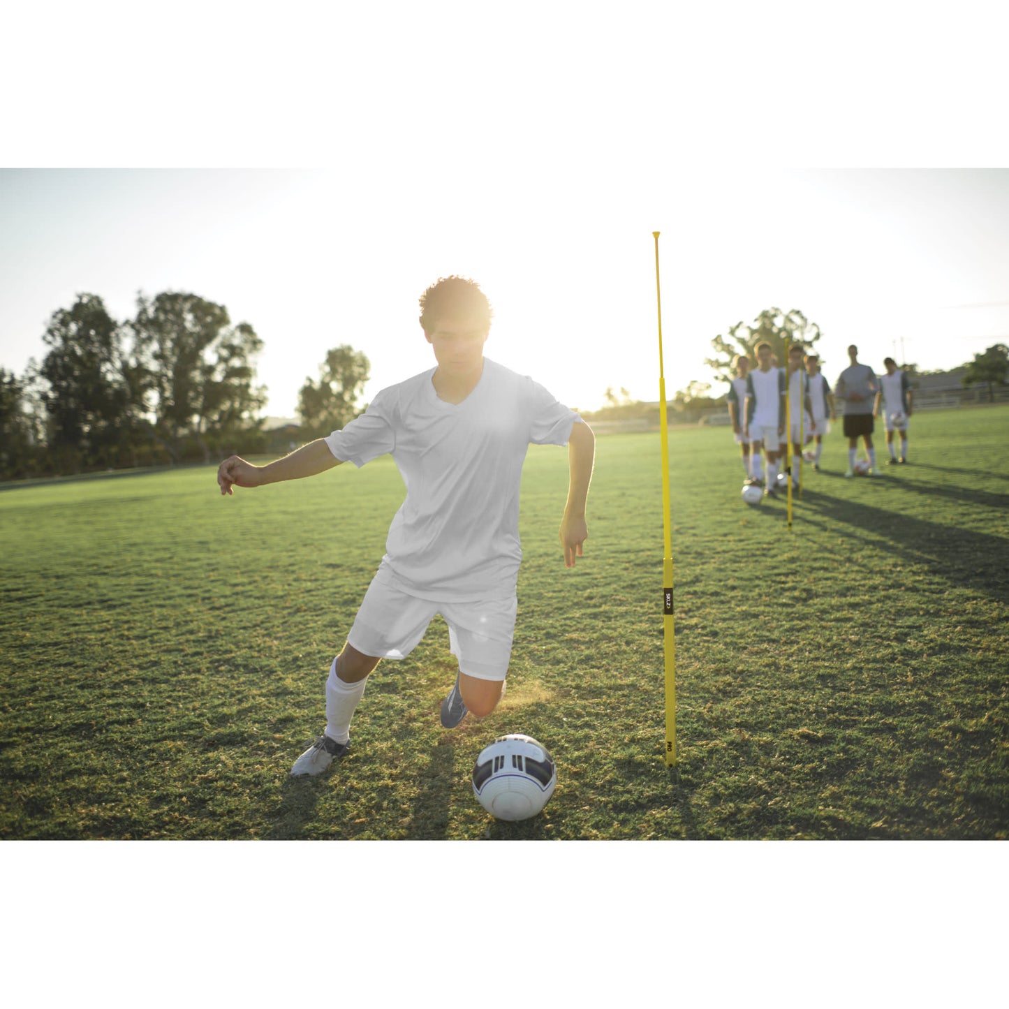 Soccer player dribbles ball during practice on grass field with teammates nearby