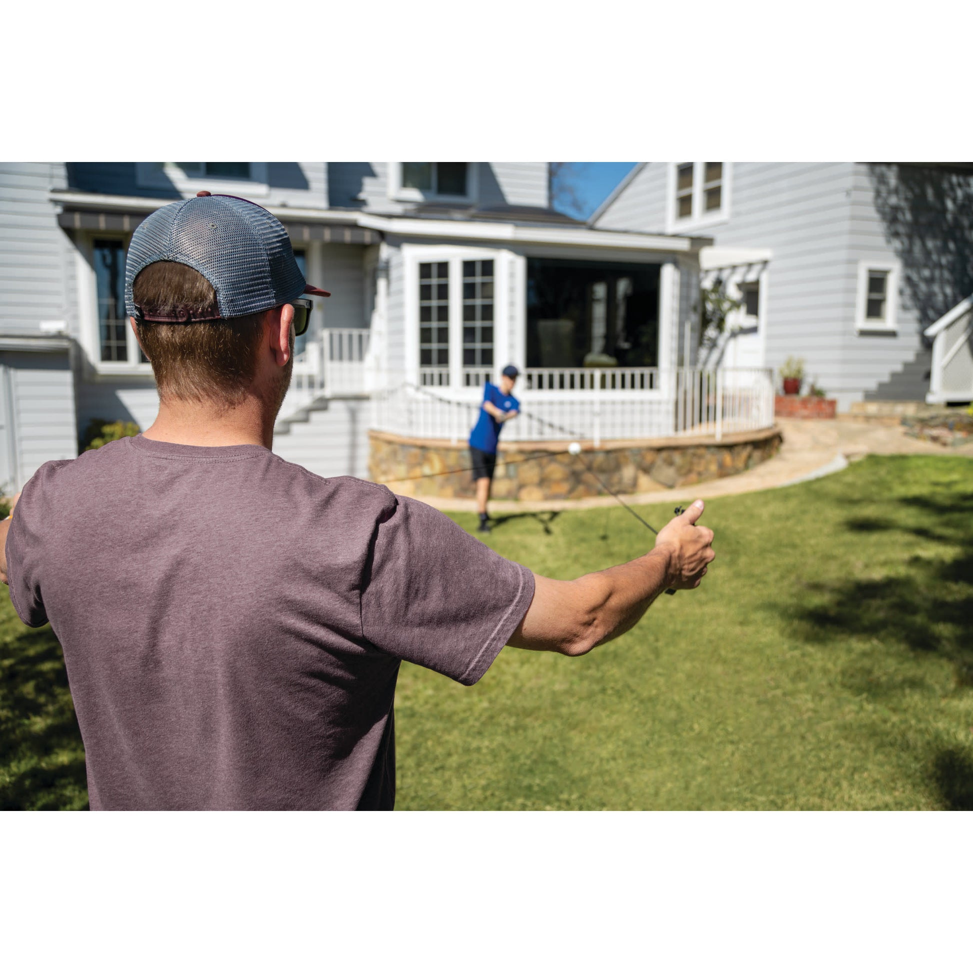 A man flys a kite in a backyard with a child playing near the house