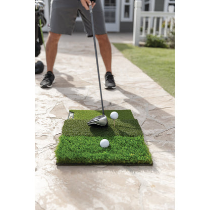 A person practices golf putting on a mini grass mat outside near a house