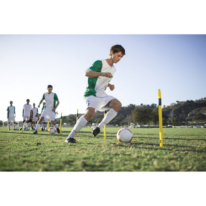 Soccer player practices dribbling around yellow poles on a grassy field during training