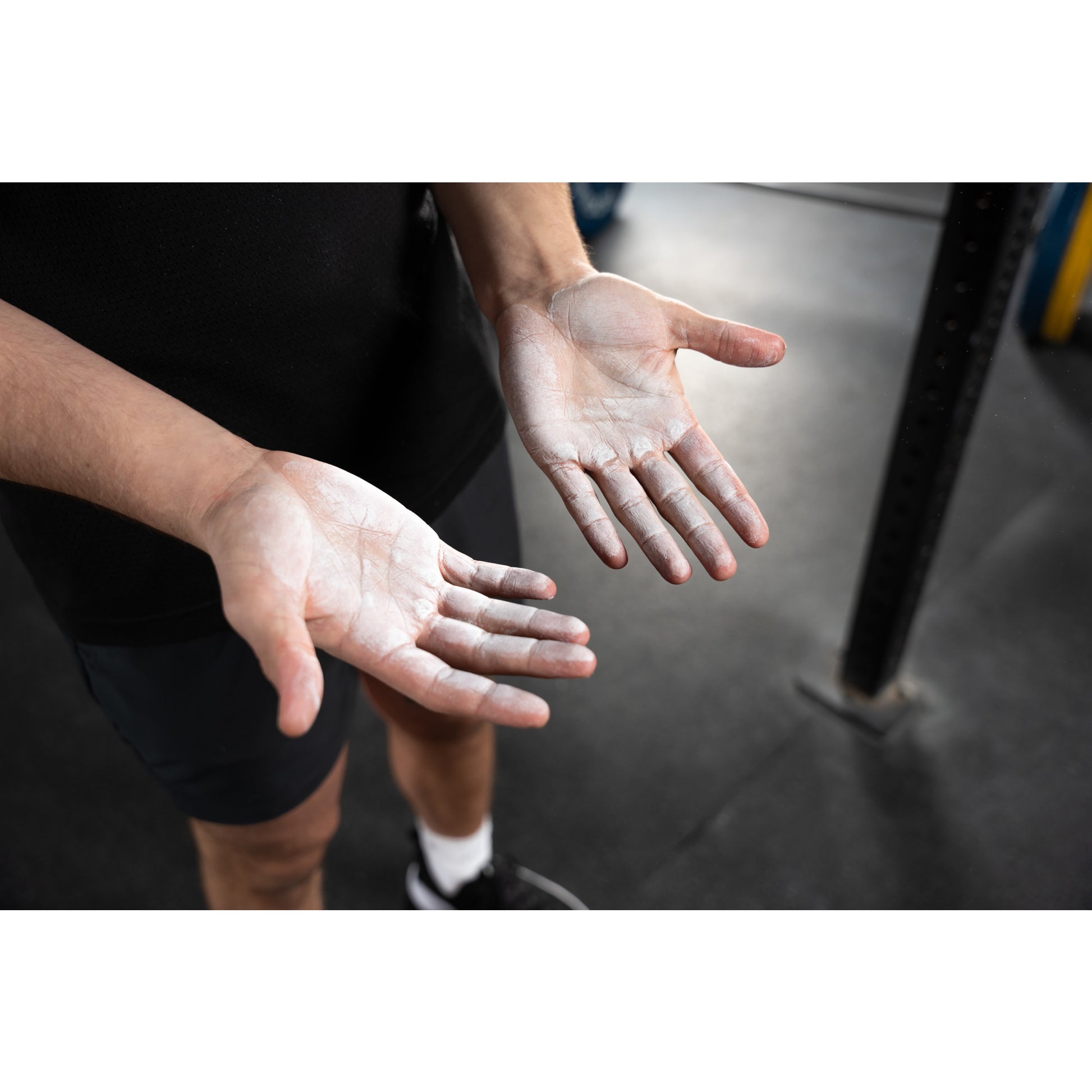 Hands covered in chalk, open wide in a gym setting with equipment nearby.