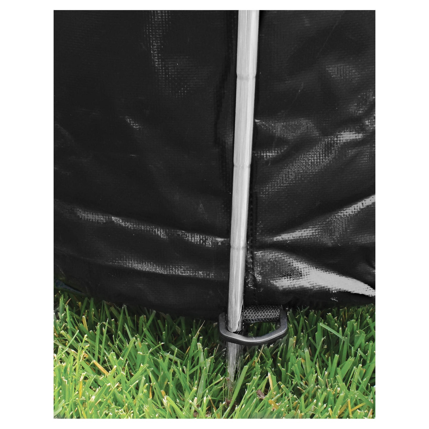 Tent stake secures black fabric in grassy outdoor environment