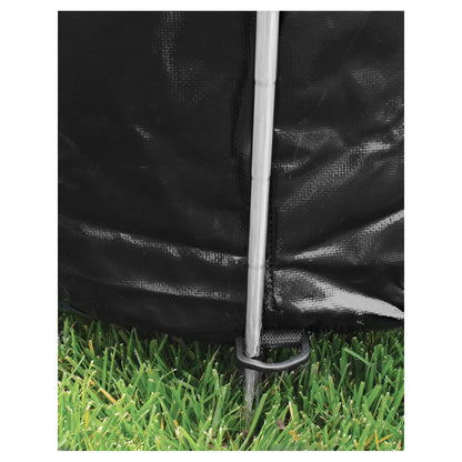Tent stake secures black fabric in grassy outdoor environment