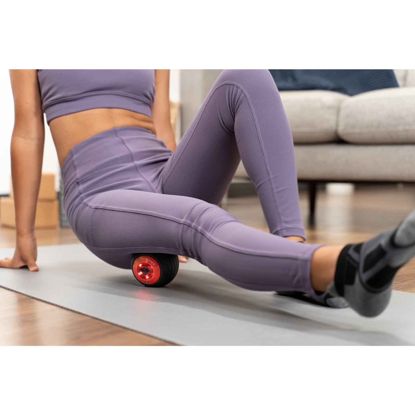 Woman uses a massage roller for muscle relaxation on a yoga mat at home.