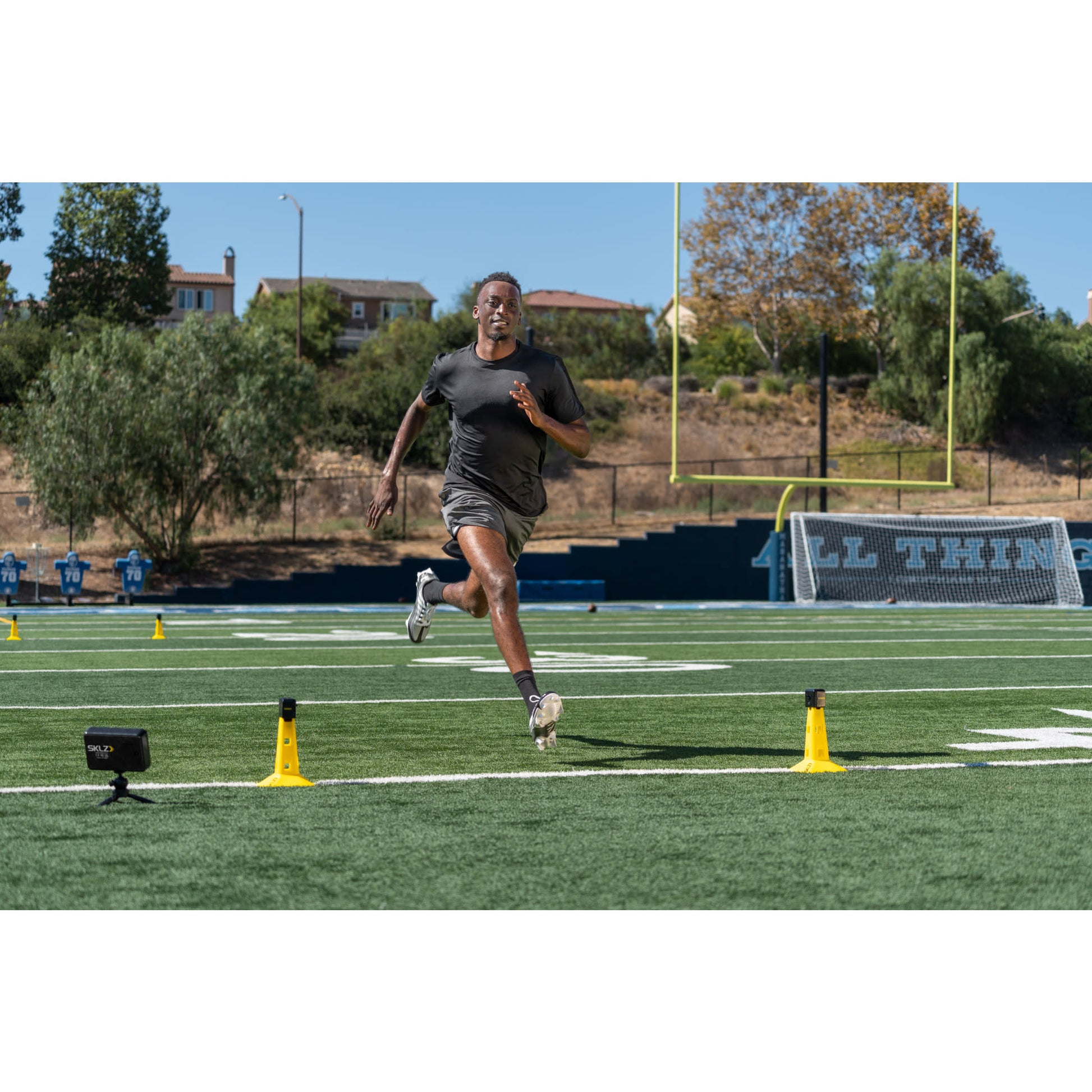 Runner trains on track with cones and timer on a football field outdoors