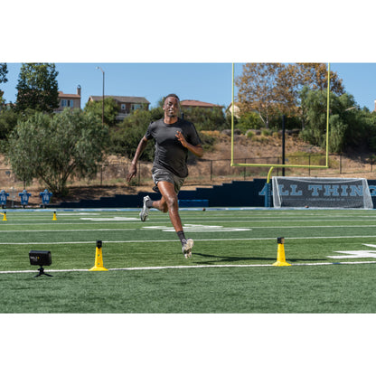 Runner trains on track with cones and timer on a football field outdoors