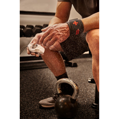 Hands squeezing chalk ball, dust cloud forming, gym setting with kettlebell on floor.