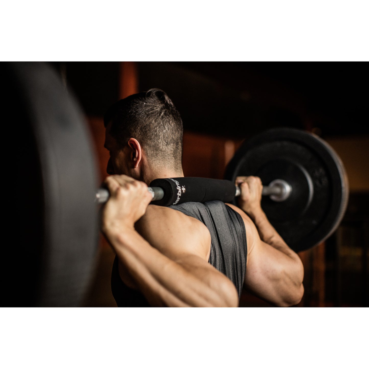 Man lifts barbell in gym, dim lighting enhances muscular focus.