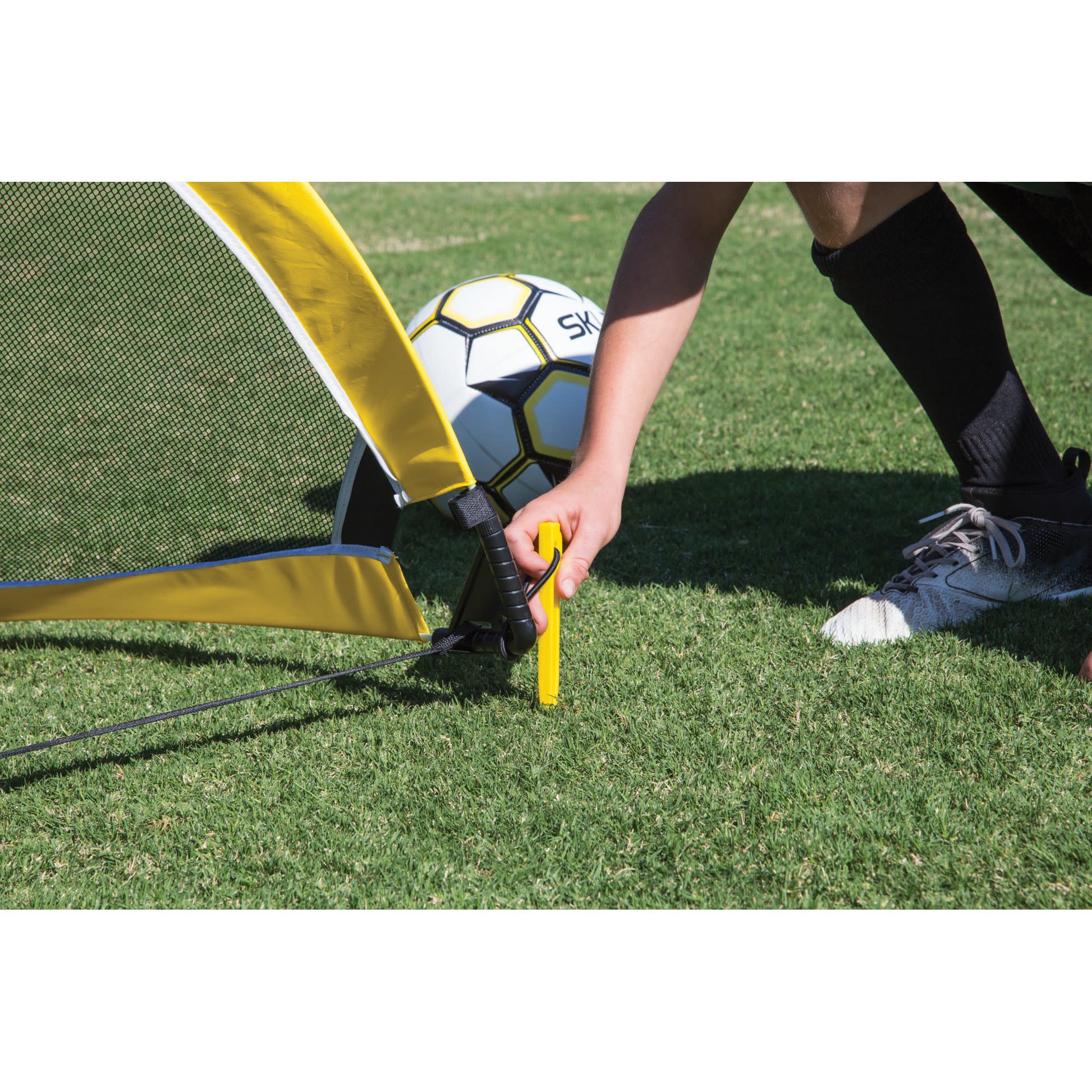 A person sets up a soccer goal on grass with a soccer ball nearby