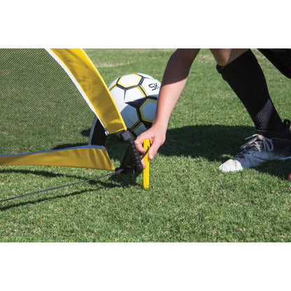 A person sets up a soccer goal on grass with a soccer ball nearby
