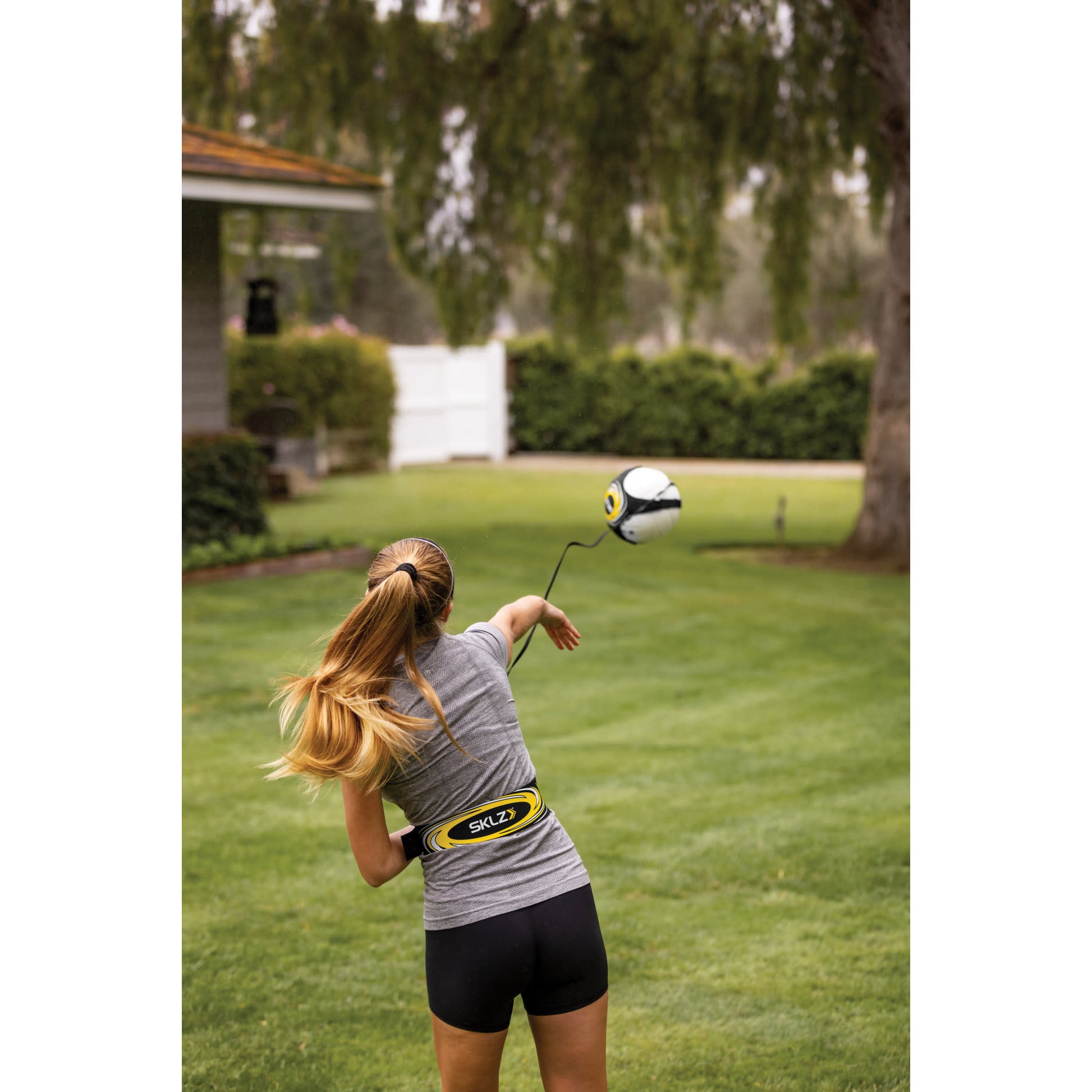 Girl swings a golf club on a lawn with a soccer ball flying through the air outdoors
