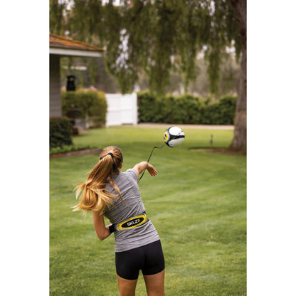 Girl swings a golf club on a lawn with a soccer ball flying through the air outdoors