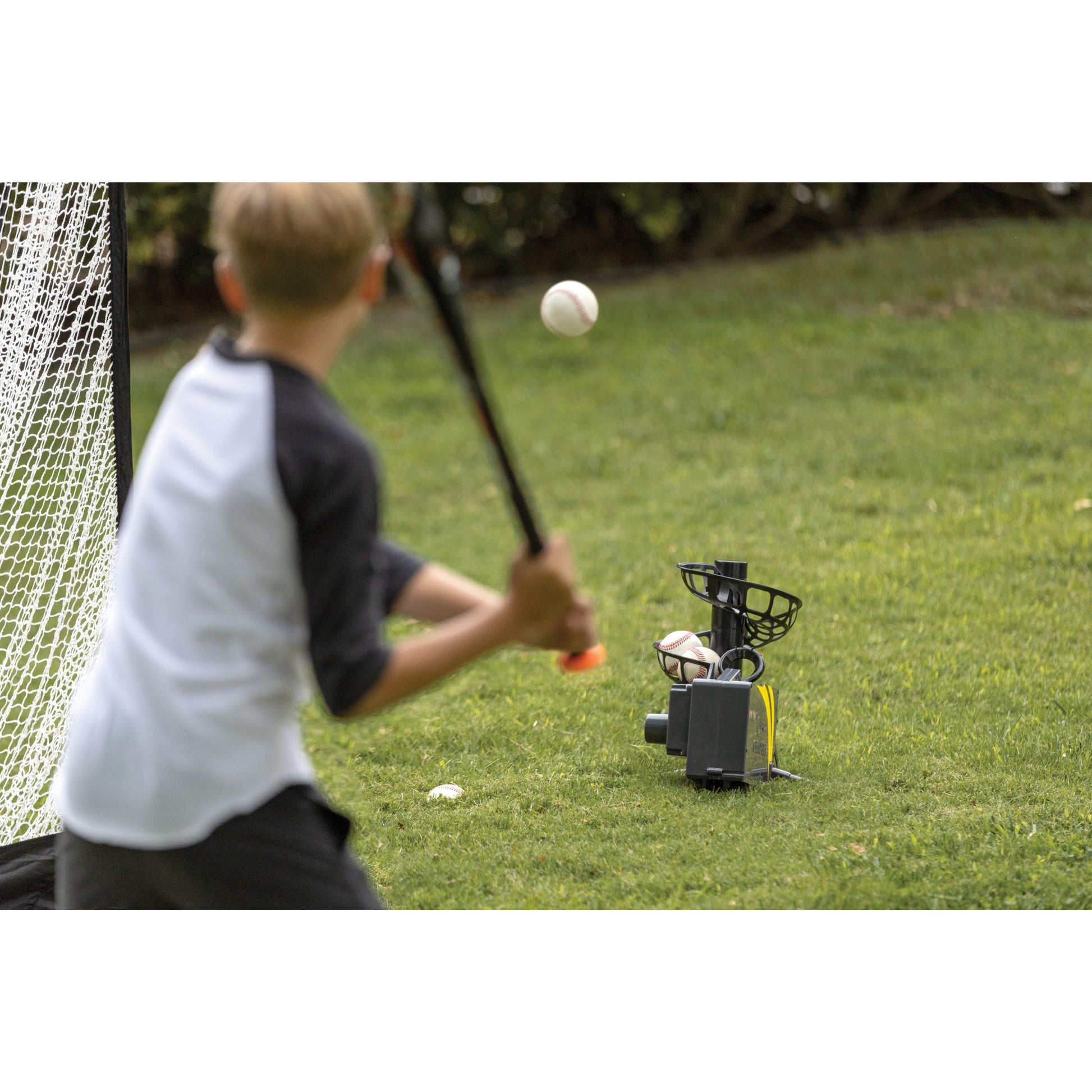 Child practicing golf swings near a ball launcher on the lawn outdoors