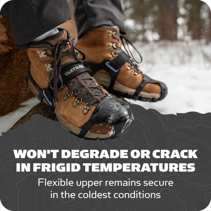 Boots with traction devices step on snow near trees.