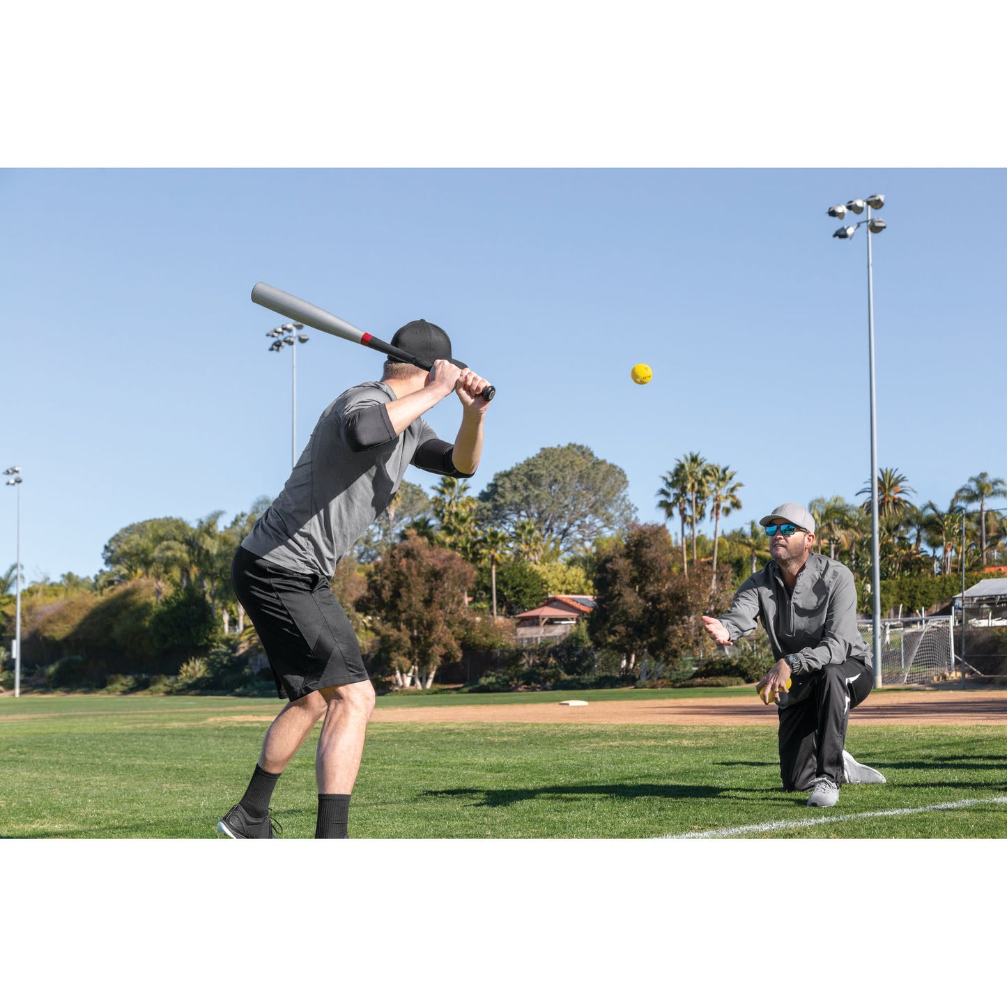 Baseball bat swings at ball during practice on a sunny outdoor field