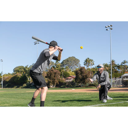 Baseball bat swings at ball during practice on a sunny outdoor field
