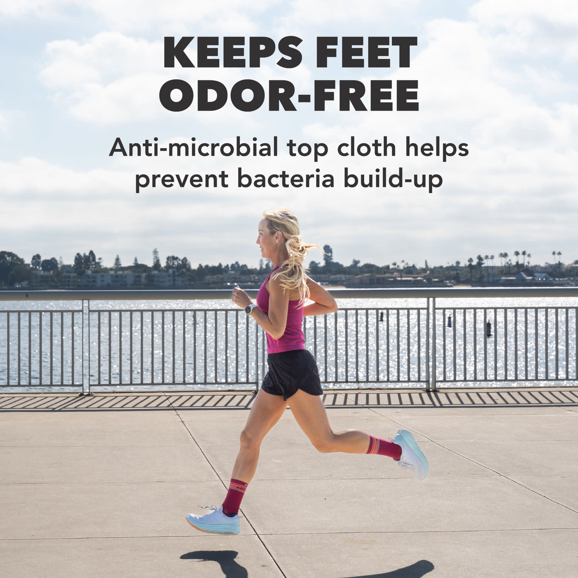 A woman runs outdoors near a body of water, wearing anti-microbial top cloths.