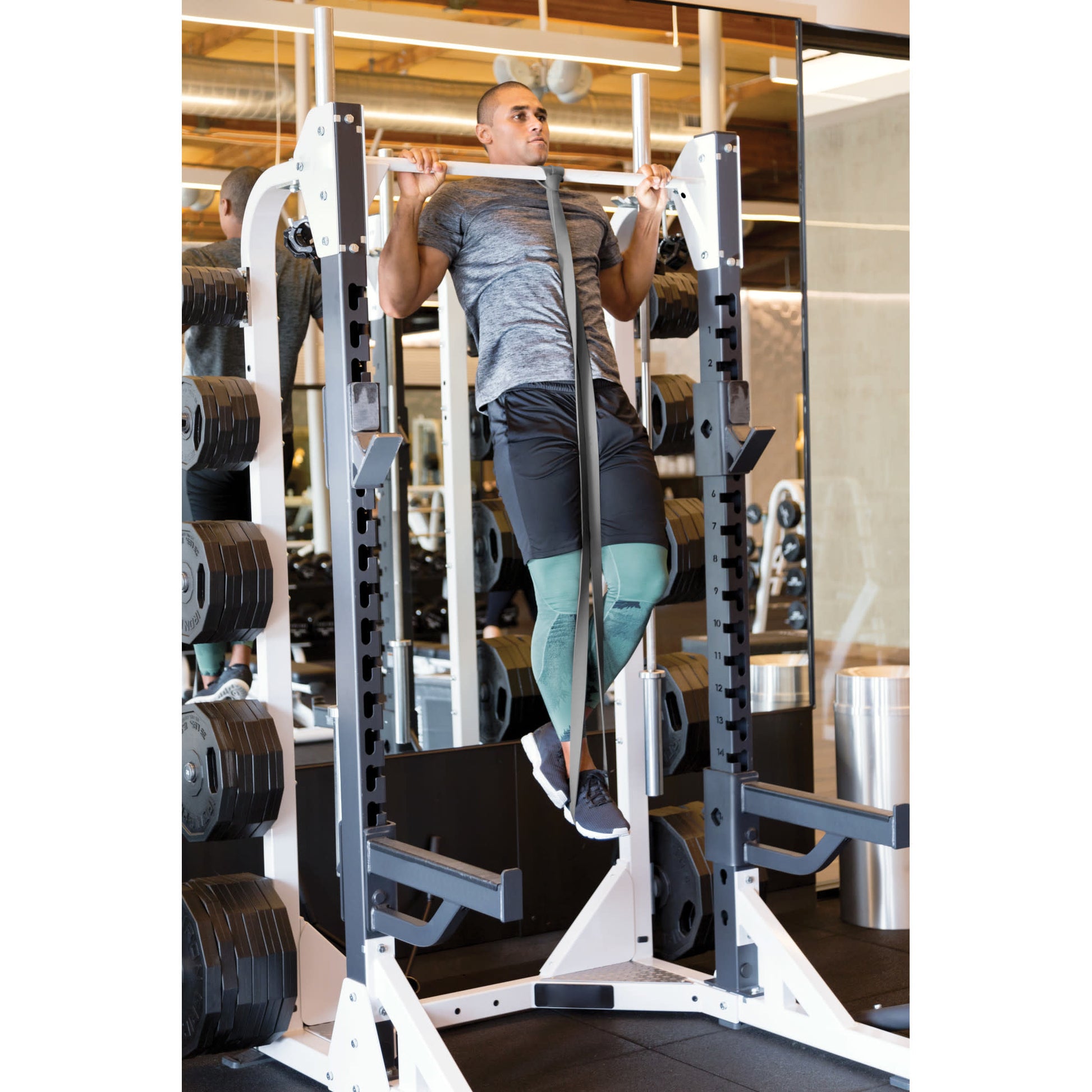 Tense man lifts on a pullup bar in a gym surrounded by weights and mirrors