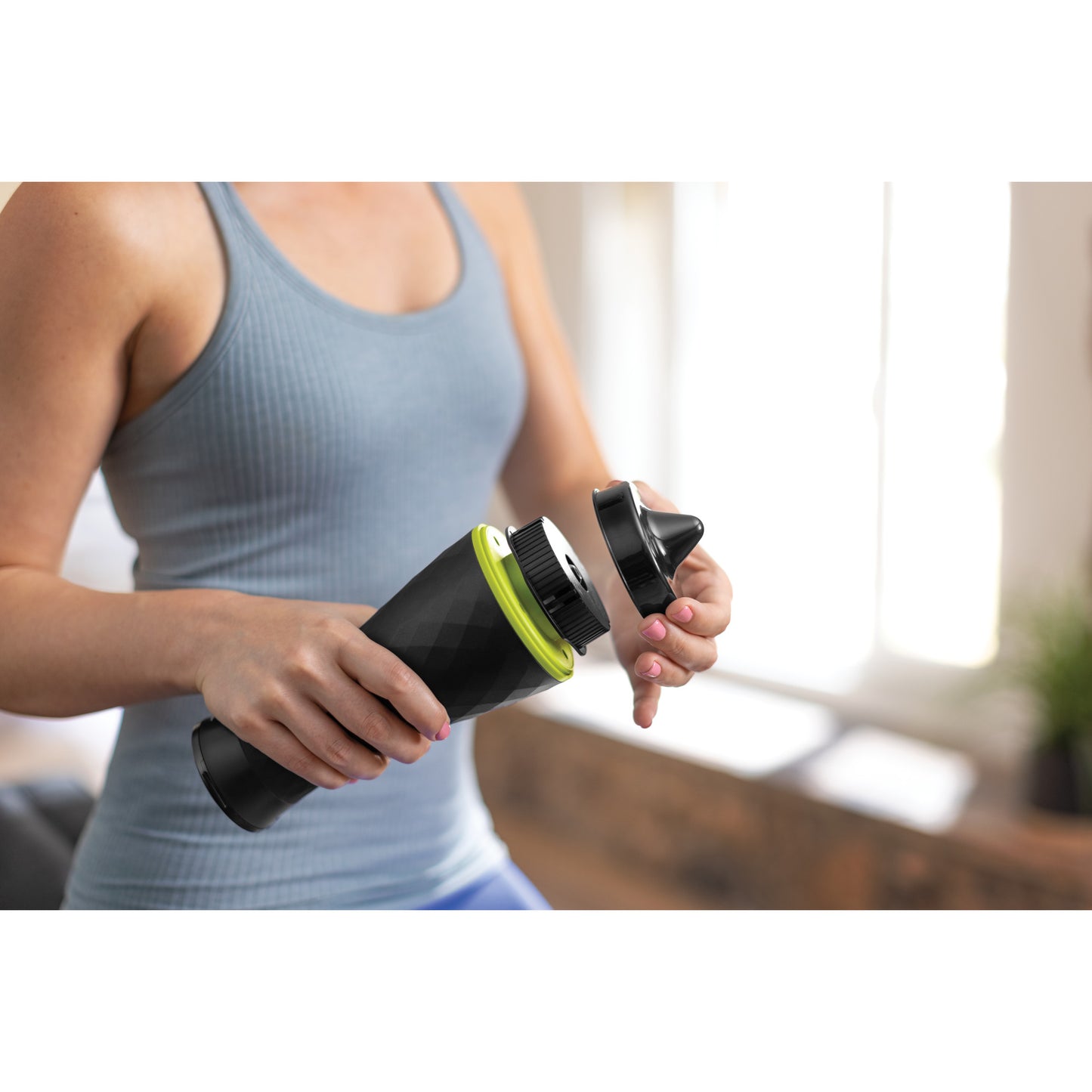 A woman holding a portable blender in a bright home, preparing to blend a drink.