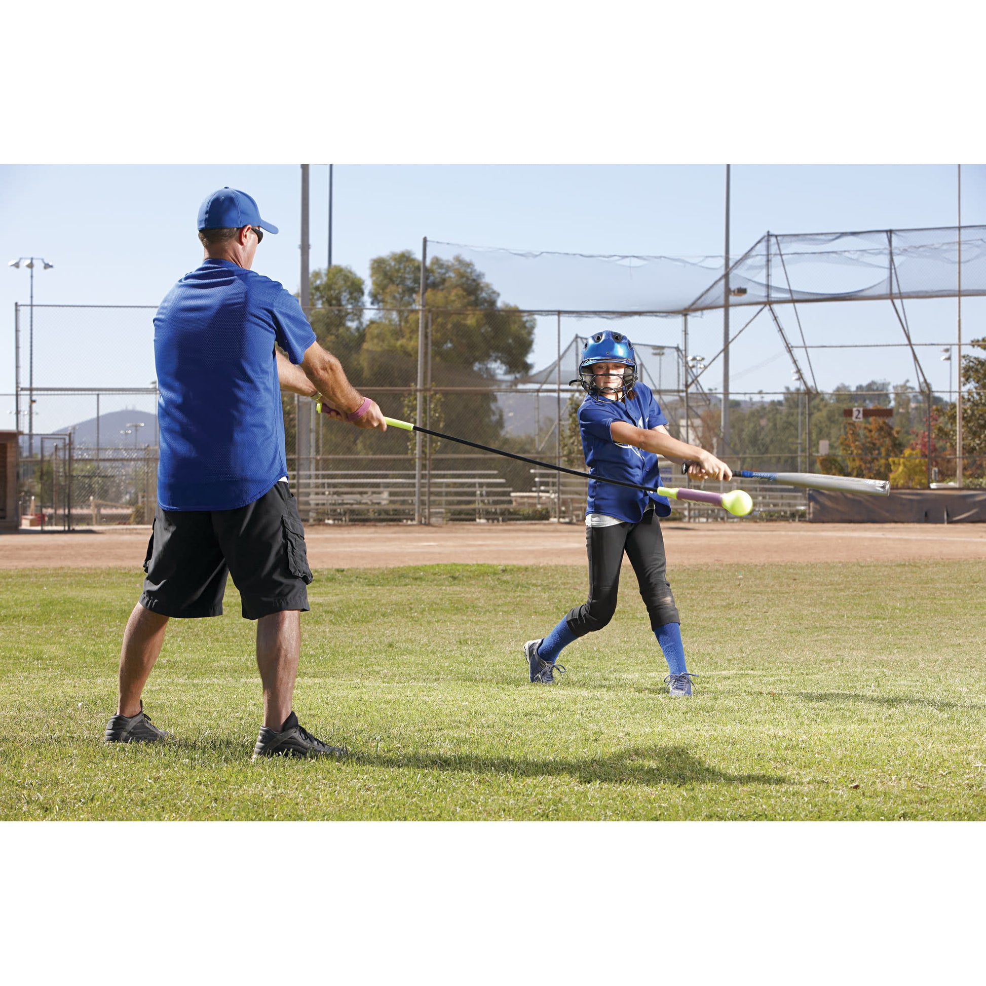 Young girl swings a bat at a ball during a baseball practice on a grassy field.
