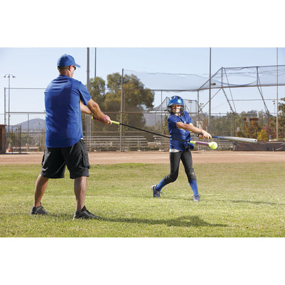 Young girl swings a bat at a ball during a baseball practice on a grassy field.